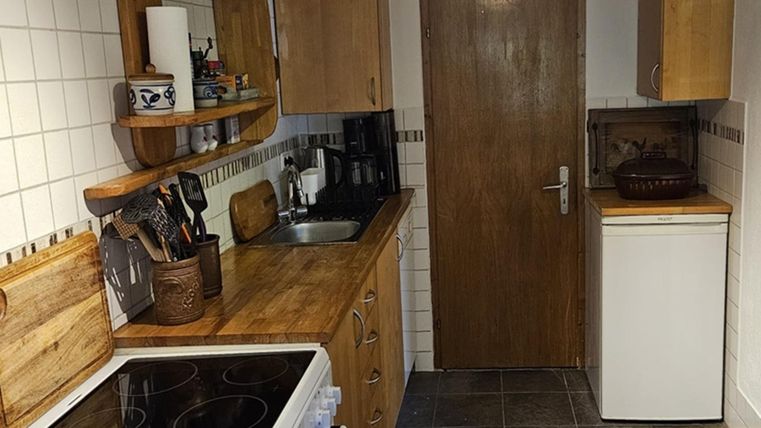 Eine gemütliche Küche mit Holzregalen und modernen Geräten. Die Wände sind gefliest, und es gibt einen Kühlschrank neben einer Tür.