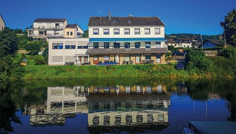 Ein ruhiges Gebäude am Wasser mit einer klaren Reflexion im See. Die Umgebung ist grün und einladend.