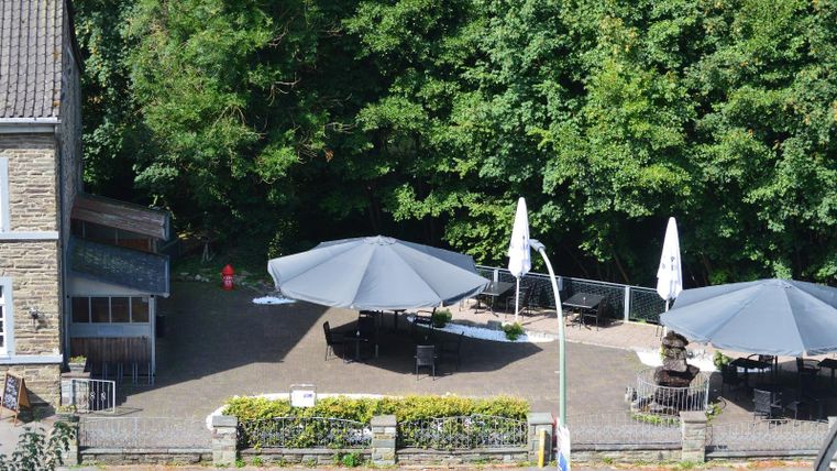 Eine gemütliche Terrasse mit großen Sonnenschirmen und Sitzgelegenheiten. Im Hintergrund sind grüne Bäume zu sehen.