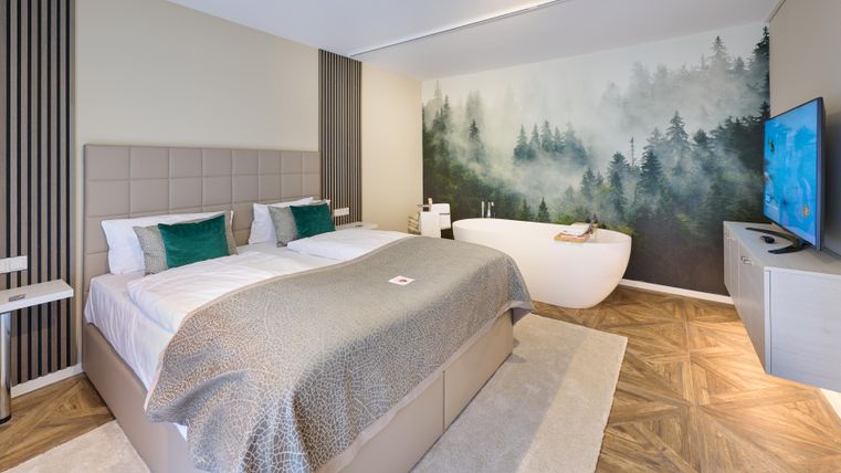 Ein modernes Hotelzimmer mit einem großen Bett und einem stilvollen Badewanne. Die Wand ist mit einem beruhigenden Waldmotiv dekoriert.