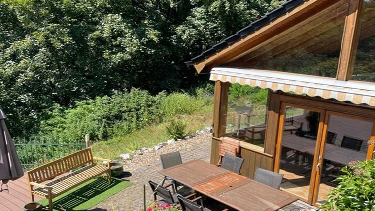Een gezellig houten huis met een terras en een eettafel buiten. Omgeven door veel groen en bomen, biedt het een rustige toevluchtsoord.