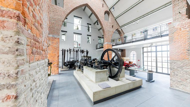 Ein historischer Raum mit Backsteinmauern und hohen Decken. In der Mitte steht eine große Maschine auf einem Betonblock.