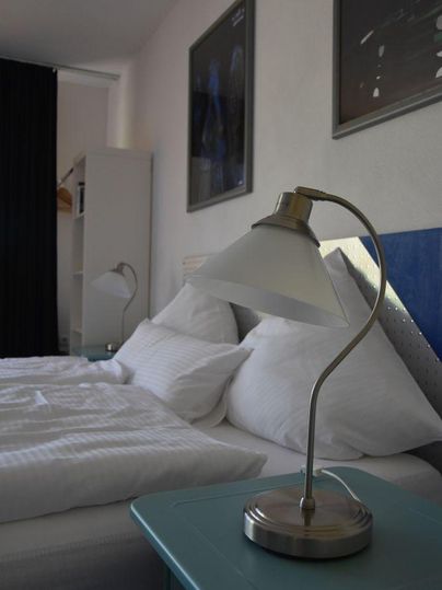 Ein modernes Schlafzimmer mit einem Doppelbett und zwei Kissen. Eine stilvolle Tischlampe steht auf einem blauem Nachttisch.