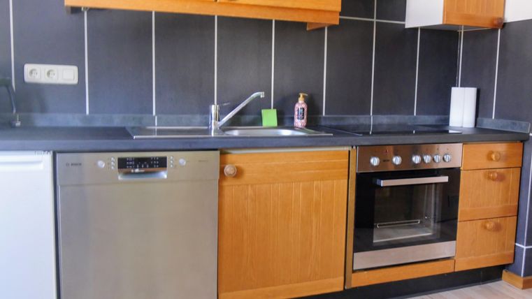 Eine moderne Küche mit Holzschränken und Edelstahlgeräten. Die Fläche ist ordentlich und gut organisiert, mit einem Herd, einer Spüle und einem Geschirrspüler.