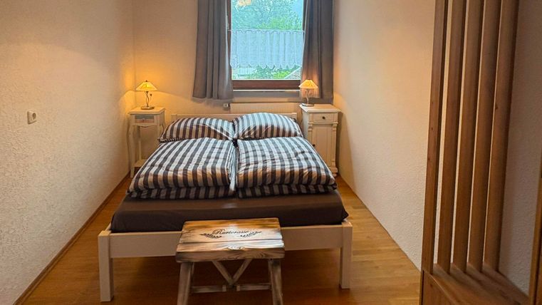Une chambre confortable avec un lit double et des couettes à carreaux. Les teintes chaudes du bois et les fenêtres créent une atmosphère accueillante.