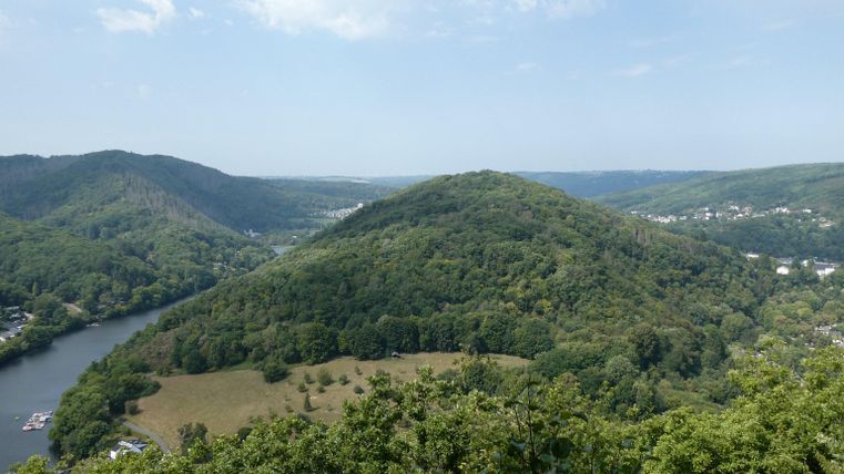 Eine weite Landschaft mit sanften Hügeln und einem Fluss. Die Umgebung ist grün und bewaldet, unter einem klaren Himmel.