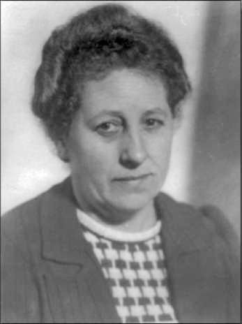 The picture shows a woman with curly hair and a neutral expression. She is wearing a striped sweater and a jacket.