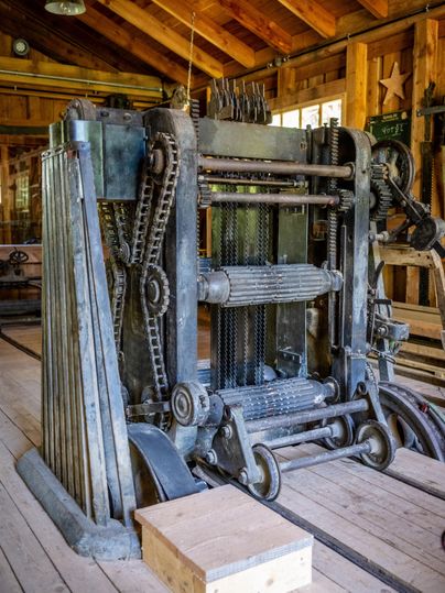 Une vieille presse à imprimer se trouve dans un bâtiment en bois. Elle montre la mécanique et le design artisanal des temps passés.