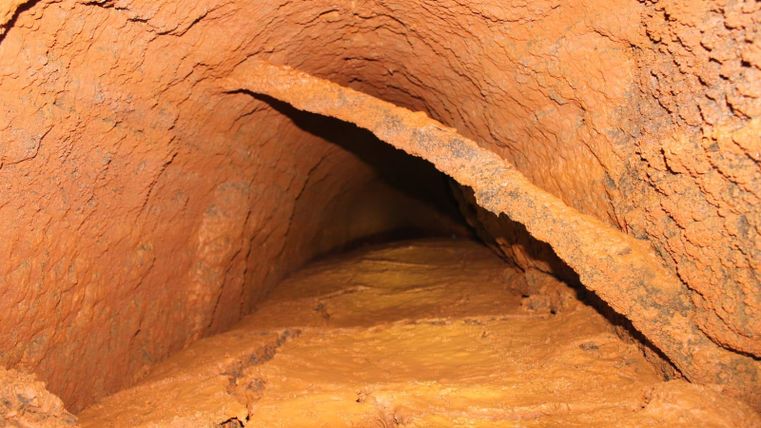 Un tunnel étroit aux parois brun-rougeâtre et à la surface rugueuse. Le sol est constitué d'un matériau minéral qui semble coincé entre les parois.