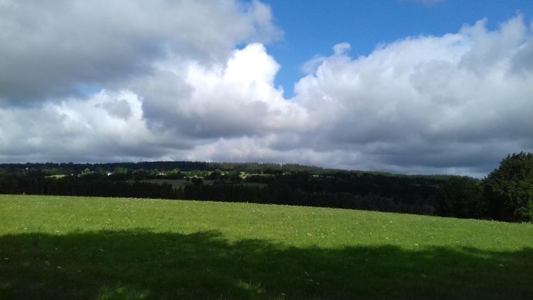 A wide green meadow under a cloudy sky. Gentle hills can be seen in the background.