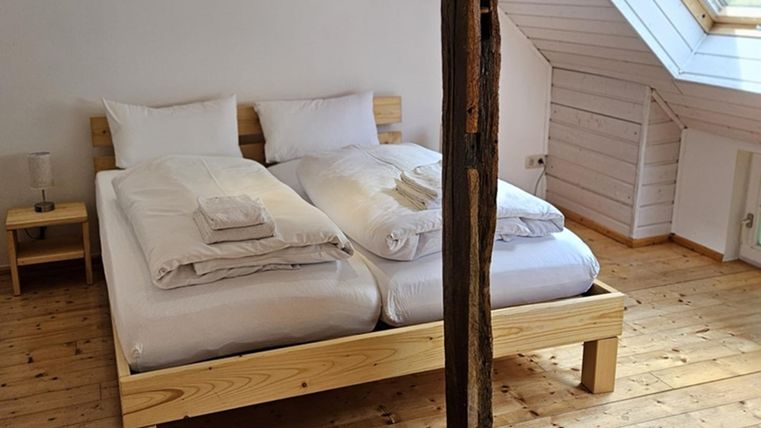 Ein gemütliches Schlafzimmer mit einem Doppelbett und Holzfußboden. Das Zimmer hat große Fenster mit viel Tageslicht.