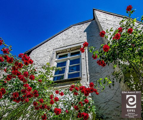Ein charmantes Haus mit einem weißen Putz und einem schönen Fenster. Rote Rosen umrahmen die Fassade und der Himmel ist strahlend blau.