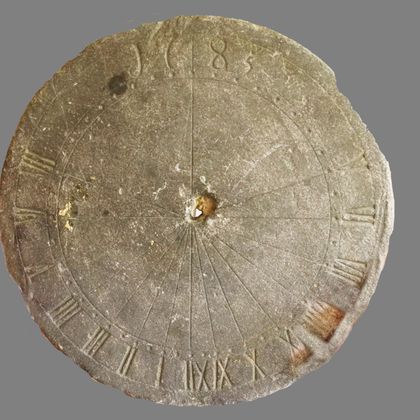 An old stone sundial with roman numerals and a simple design. The dial displays the hour lines and has a central opening for the gnomon.