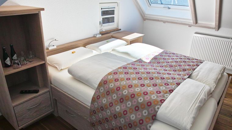 Ein gemütliches Schlafzimmer mit einem Doppelbett und bunten Bettdecken. Neben dem Bett steht ein Holzschrank mit einigen Accessoires.