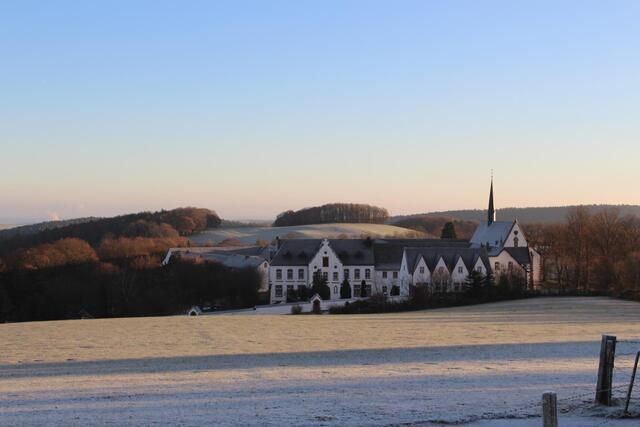 Un paysage du sud de l'Allemagne en hiver avec un champ couvert de givre et un bâtiment historique. Le ciel est clair et les arbres à l'arrière-plan sont dépouillés.