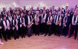 Eine Gruppe von Musikern steht zusammen und posiert für ein Foto. Sie tragen schwarze und weiße Kleidung und halten verschiedene Musikinstrumente.