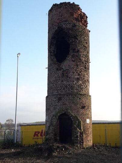 Ein alter, beschädigter Ziegelturm steht in einer offenen Landschaft. Der obere Teil ist stark verfallen und der Himmel im Hintergrund ist klar.
