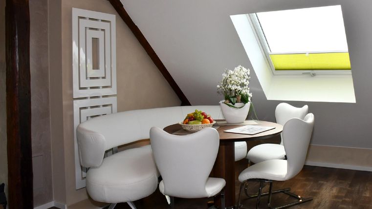 Une salle à manger élégante avec une table ronde et des chaises modernes. De grandes fenêtres permettent un maximum de lumière naturelle et créent une atmosphère lumineuse.