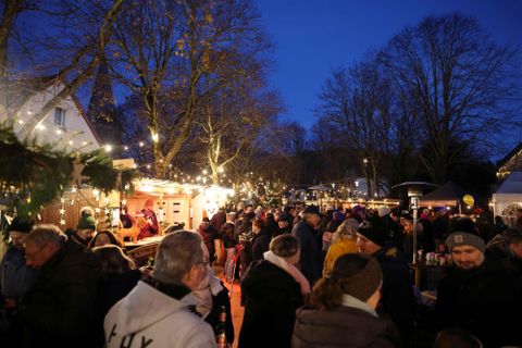 Ein festlicher Weihnachtsmarkt bei Nacht, beleuchtet von vielen Lichtern. Eine große Menschenmenge genießt die Atmosphäre und die Stände.