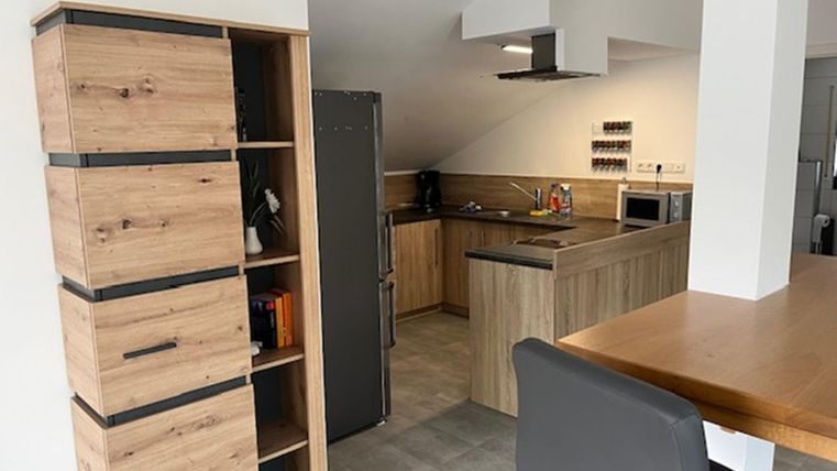 Eine moderne Küche mit Holzregalen und einer Kochzeile. Der Raum ist hell und freundlich eingerichtet.