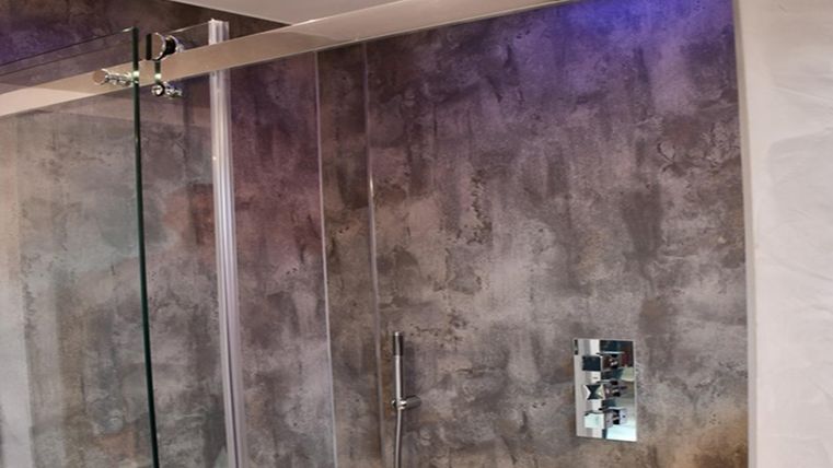 Une salle de bain moderne avec une douche en verre et des murs en béton stylés. L'éclairage au plafond crée une atmosphère agréable.