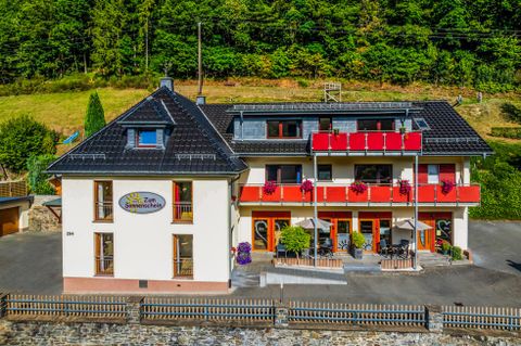Ein charmantes Hotel mit roten Balkonen in einer grünen Umgebung. Die Fassade wirkt einladend und freundlich.