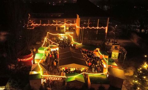 Eine festlich beleuchtete Veranstaltung im Freien mit zahlreichen Menschen. Bunte Lichter und Stände schaffen eine einladende Atmosphäre.