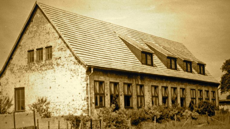 An old, rustic building with a sloped roof and several windows. The image has a sepia-toned look that evokes a sense of nostalgia.