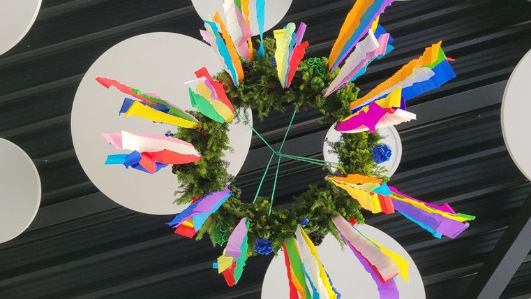 Eine bunte Dekoration mit vielen farbigen Papierstreifen und einem grünen Kranz. Sie hängt von der Decke und bringt Freude in den Raum.