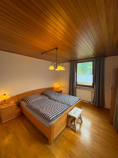 Une chambre confortable avec un lit double et un plafond en bois. Il y a des tables de nuit, une lampadaire et une fenêtre avec des rideaux.