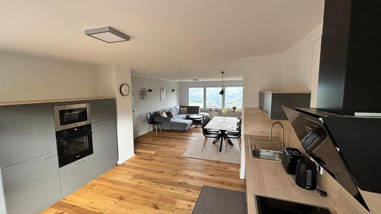 Een moderne keuken met houten vloeren en elegante apparaten. Op de achtergrond is een gezellige woonruimte te zien met een eettafel en een mooi uitzicht.