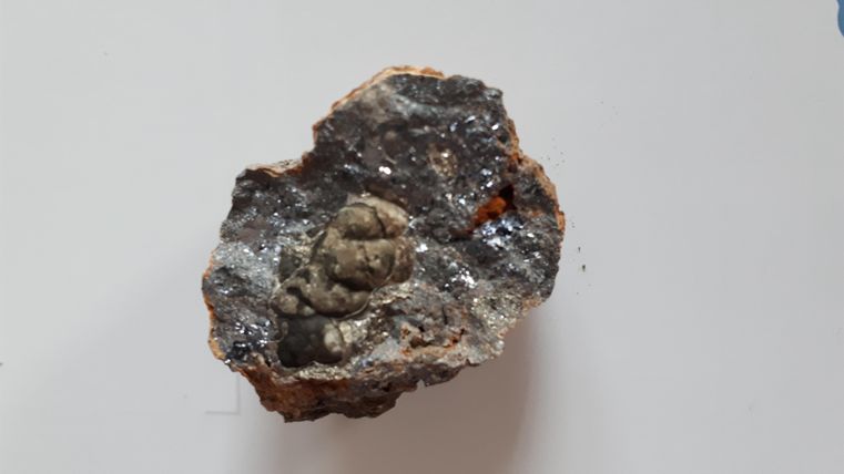 Un morceau de roche avec une petite figure encapsulée à l'intérieur. La surface est rugueuse et montre différentes structures minérales.
