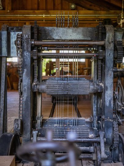 Une ancienne machine à tisser en métal se trouve dans une pièce rustique. Elle montre les pièces mécaniques et les fils utilisés pour la fabrication des tissus.