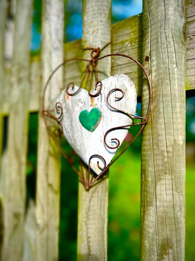 Ein hängendes Herz aus Holz mit einem grünen Herzsymbol. Es ist an einem Holzzaun befestigt und umgeben von einem grünen Hintergrund.