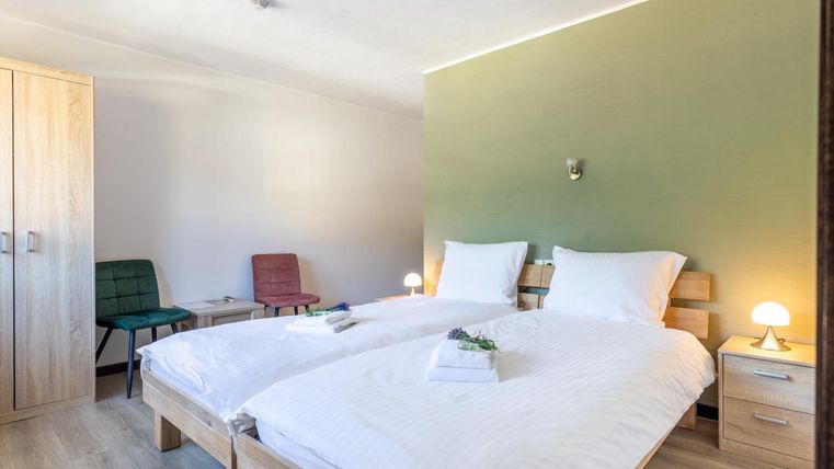 Ein modernes Schlafzimmer mit zwei Einzelbetten und Holzdecken. Der Raum hat eine beruhigende grüne Wand und gemütliche Stühle.