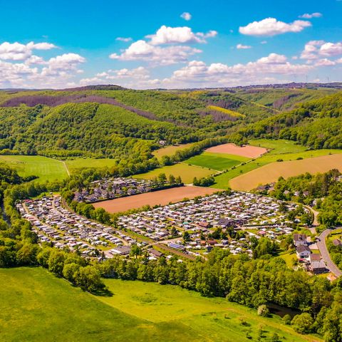 Blick von der Burg Nideggen: Eine malerische Landschaft mit sanften Hügeln und grünen Feldern. Der Campingplatz liegt eingebettet zwischen dem Nationalpark Eifel und der Rur, die am Campingplatz entlang fließt.