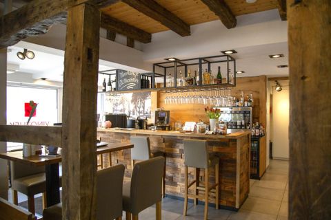 Eine gemütliche Bar mit einem Holztheke und modernen Stühlen. Die Einrichtung kombiniert rustikalen Charme mit einer einladenden Atmosphäre.