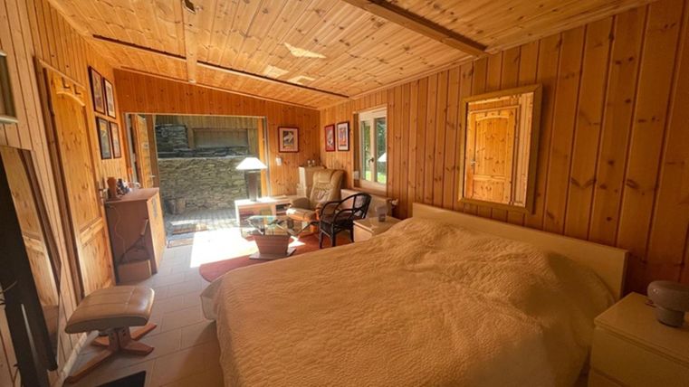 Een gezellige slaapkamer met houten wandbekleding en een groot bed. Er is een raam dat uitkijkt op een groene oase, evenals een paar meubelstukken die de ruimte uitnodigend maken.