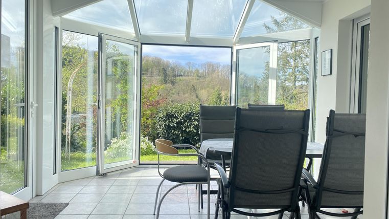 Een gezellige wintertuin met open ramen. Op de achtergrond zijn groene planten en een rustige omgeving te zien.