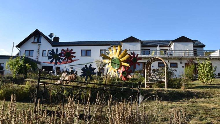 Ein großes Wohnhaus mit bunten Windrädern im Vordergrund. Der Garten ist grün und gepflegt, ideal für entspannte Tage im Freien.