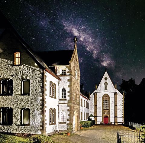 Ein historisches Gebäude mit einer Kirche bei Nacht, unter dem Sternenhimmel. Die Milchstraße ist sichtbar und verleiht der Szene eine magische Atmosphäre.