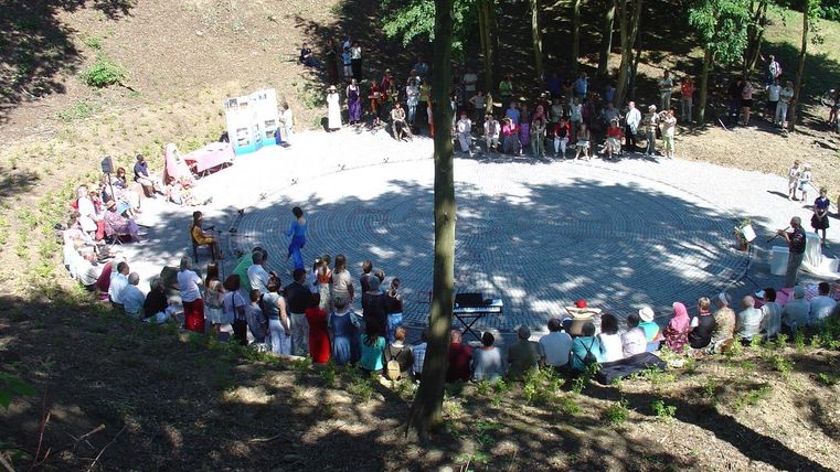 Eine Gruppe von Menschen versammelt sich in einem Wald für eine Veranstaltung. Sie stehen an einem runden Platz, umgeben von Bäumen.