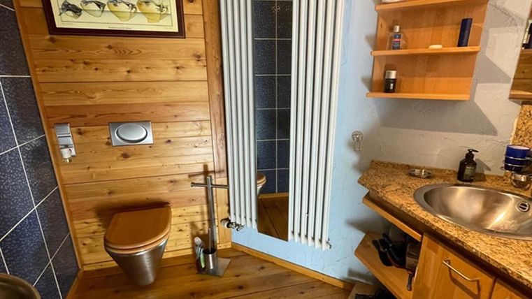 Een modern badkamer met houten panelen en een wastafel. Er is een douche en een plank met verzorgingsproducten.
