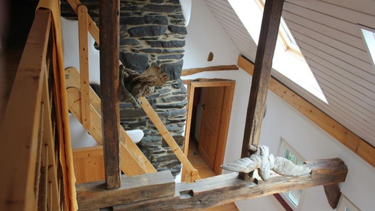 Ein helles, modernes Chalet mit Holzbalken und einem Steinkamin. Der Raum hat große Fenster und eine einladende Atmosphäre.