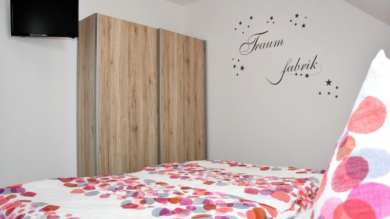 Une chambre cozy avec un lit et des coussins colorés. Sur le mur se trouve l'inscription "Usine de rêves" et il y a une télévision.