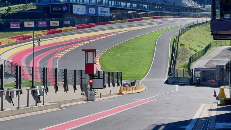 Eine Rennstrecke mit einer langen Kurve und einem Blick auf die Tribüne. Im Hintergrund sind Bäume und ein klarer Himmel sichtbar.