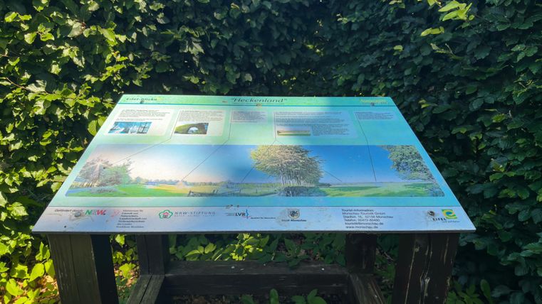 Een informatiebord over de regio "Heckenland". Het toont een beschrijving van het landschap met tekst en afbeeldingen.