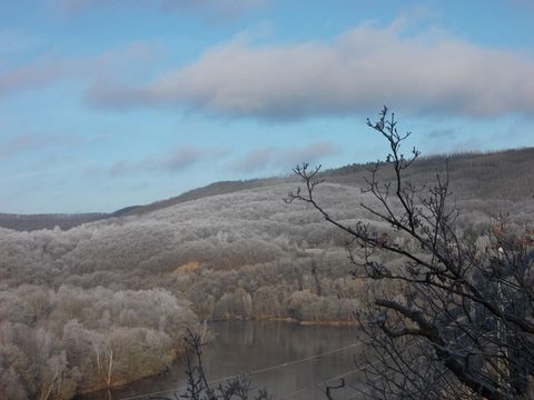 Eine verschneite Landschaft mit gefrorenen Bäumen und einem ruhigen Fluss im Vordergrund. Der Himmel ist klar mit einigen Wolken.