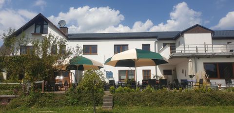 Ein gemütliches Gasthaus mit Sonnenschirmen und einer einladenden Terrasse. Die Umgebung ist grün und es gibt einen klaren blauen Himmel.