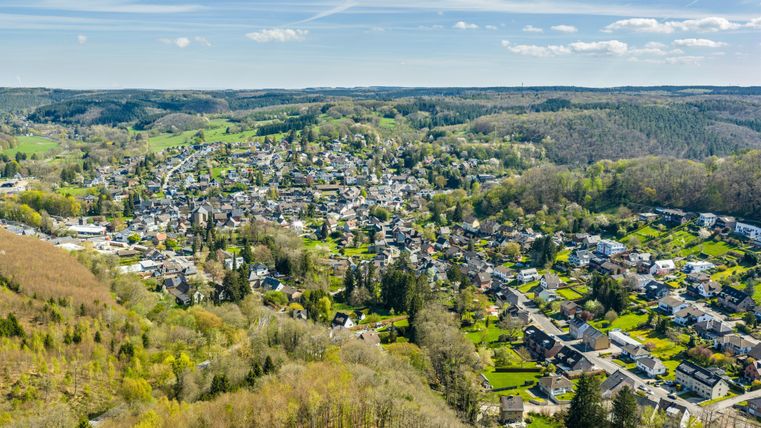 Een schilderachtig uitzicht op een rustig dorp omgeven door groene heuvels en bossen. De huizen zijn goed verdeeld en het landschap lijkt uitnodigend en vredig.
